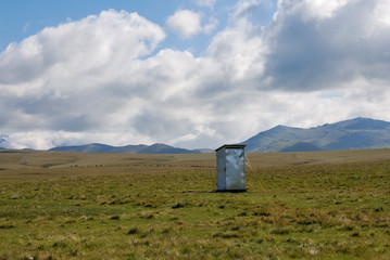 Kyrgyz steppe, near Songkol lake. Metal outhouse in the middle of pasture and mountains in far background. Kyrgyzstan