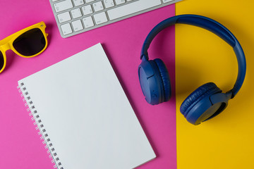 Flat lay composition with headphones, sunglasses, notepad and keyboard on a yellow purple background. Modern students.