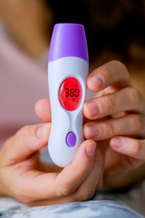 Feverish infrared thermometer showing body temperature. A woman is sick with a fever.