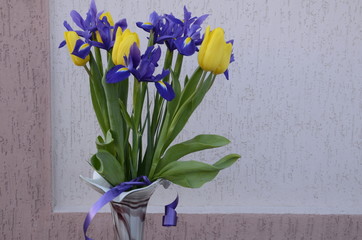 On a light background a bouquet of fresh flowers, blue irises and yellow tulips.