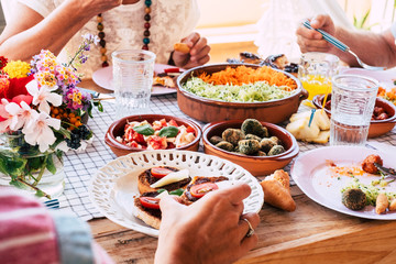 Close up of table full of fresh vegetarian vegan food with group of people eating together in friendship or parentship at home or restaurant - concept of healthy lifestyle an coloured food