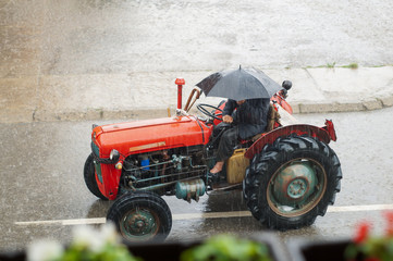 A farmer drives a large red tractor across flood waters in the street.