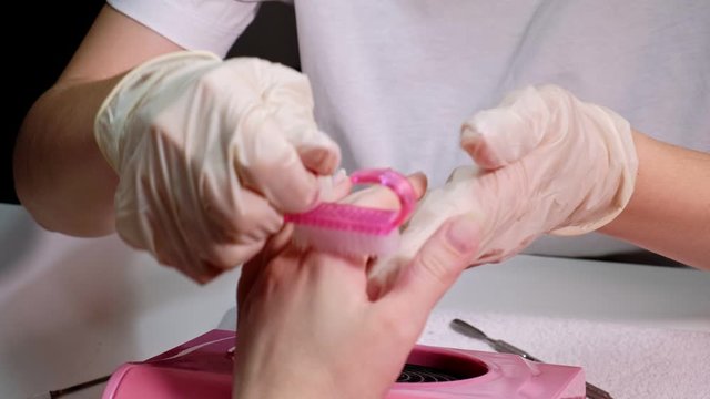 A girl gets a manicure in a beauty salon. Nail brush. Close up.Women's hands in the process of manicure, removing dirt with a pink brush