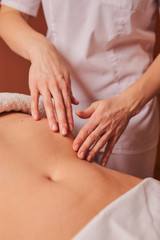 The specialist makes the girl a therapeutic massage of the abdomen on the table in the massage parlor.