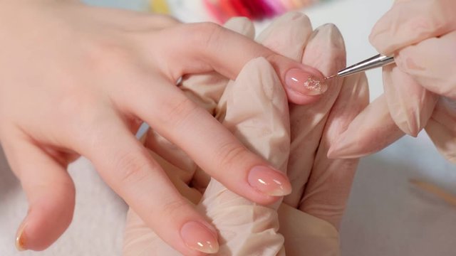 The manicure master applies a shiny nail Polish to the client's nails in a beauty salon. drawing a heart on the client's nails. Close up.