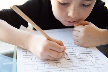 Schoolboy  writing letters. Close-up  pencil in the hand of child. Boy  learning to write letters at the table. A home distance learning.
