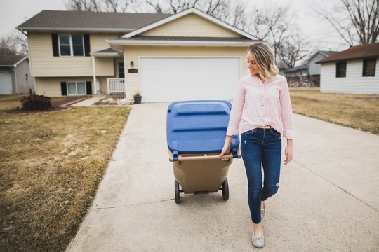 Young woman pulling recycling bin down driveway