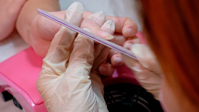 The manicure master makes the shape of the client's nail using a nail file. The concept of beauty and nail care. Close up