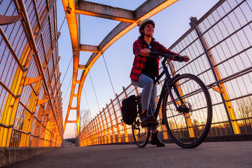 Caucasian Woman Riding a Bicycle on a Pedestrian Bridge over the Highway during a sunny sunset....
