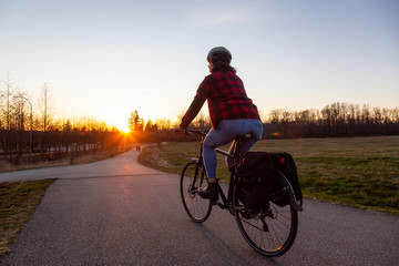 Caucasian Woman Riding a Bicycle on a Pedestrian Path during a sunny sunset. Taken in Surrey, Vancouver, British Columbia, Canada.