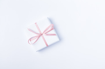 White gift box with pink ribbon on white background. Flat lay. Copy space