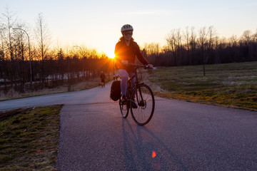 Caucasian Woman Riding a Bicycle on a Pedestrian Path during a sunny sunset. Taken in Surrey, Vancouver, British Columbia, Canada.