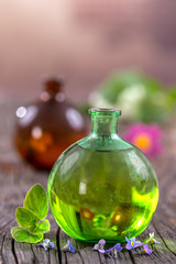 Alternative Medicine: Essential oil, on glass flask with fresh herbs and flowers on wooden background