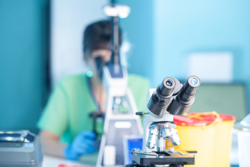 Female professional in uniform, hands in gloves. Work with light microscope in research laboratory,...