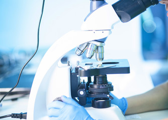 Female professional in uniform, hands in gloves. Work with light or fluorescent microscope in research laboratory or test lab. Histology, histopathology, microscopic analysis of patients biopsy.