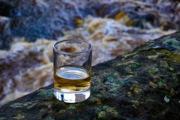 Scotch single malts or blended whisky spirits in glasses with water of river Spey on background,...
