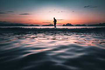 Man silhouette in the sea at  sunset with red and blue sky looking at the horizon