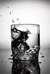 an ice cube is thrown into a glass of water, water splashes fly from a glass of water