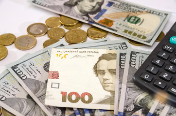 Fototapeta premium 100 hryvnia, coins and part of a calculator among dollars on white. Concept of inflation, financial crisis. Close-up. Money background.