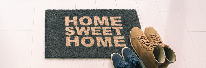 Home sweet home entrance door mat at condo floor with couples pairs of shoes moving in together....