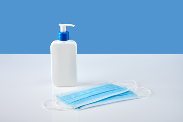 White antiseptic bottle with dispenser and two blue medicine masks on white acrylic table, blue...