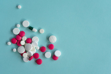 White and red pills of various shapes scattered on a blue background. Coronavirus, treatment, pills, medicine, pandemic, virus, disease. For the text. Top view, copy space.