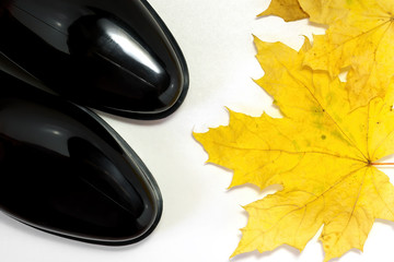 Black rubber boots and a maple leaf on a white background, top view.