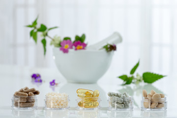 Bottle of pills food suplements healthy medicine, medication health care treatment additives pharmacy with ceramic white mortar with medicinal fresh plants on background