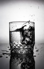 an ice cube is thrown into a glass of water, water splashes fly from a glass of water