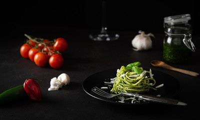 Spaghetti z sosem pesto z zielonym sosem genueńskim ze świeżymi pomidorami na czarnej płycie i czarnym tle z bocznym światłem - 333537817