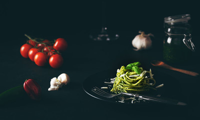 Spaghetti z sosem pesto z zielonym sosem genueńskim ze świeżymi pomidorami na czarnej płycie i czarnym tle z bocznym światłem - 333537830
