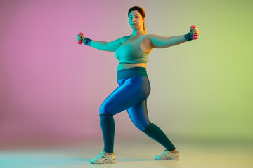 Fototapeta na wymiar Young caucasian plus size female model's training on gradient purple green background in neon light. Doing workout exercises with weights. Concept of sport, healthy lifestyle, body positive, equality.