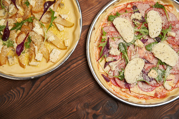 Two raw pizza with gorgonzola cheese and pear on a metal plate ready to cook