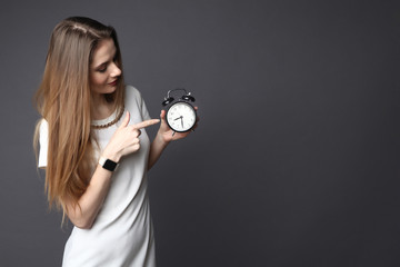 Fototapeta premium Young woman points to a retro alarm clock on grey background