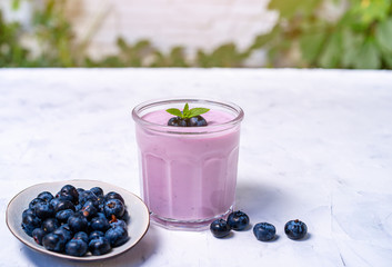 Tasty fresh blueberry yoghurt shake dessert in glass standing on white table background.