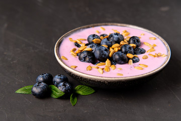 Tasty fresh blueberry yoghurt shake dessert in ceramic bowl standing on black dark table background.