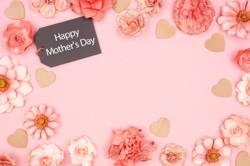 Happy Mothers Day chalkboard gift tag with frame of pink paper flowers. Top view over a pink background. Copy space.