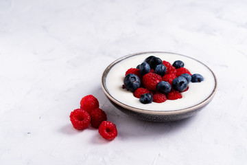 Tasty fresh blueberry raspberries yoghurt shake dessert in ceramic bowl standing on white table background.