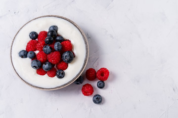 Tasty fresh blueberry raspberries yoghurt shake dessert in ceramic bowl standing on white table background.