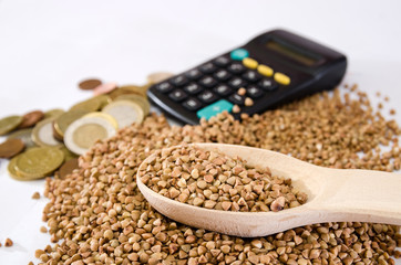 buckwheat in a wooden spoon against the background of buckwheat, a calculator and coins. The concept of a rise in price of buckwheat.
