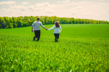 Naklejka premium A guy with a girl running holding hands on a field of green grass