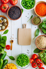 Wooden cutting board surrounded by fresh vegetables and groats