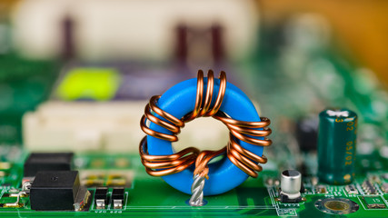 Blue toroidal induction coil on green circuit board. Computer mainboard detail. Electronic...