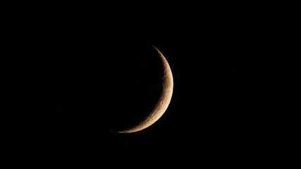 Astronomy: Tiny moon crescent full of small craters in the dark sky of the night.