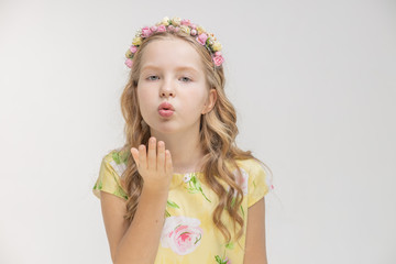 Portrait of a cute little girl sending an air kiss, standing in a pink dress on an isolated white background