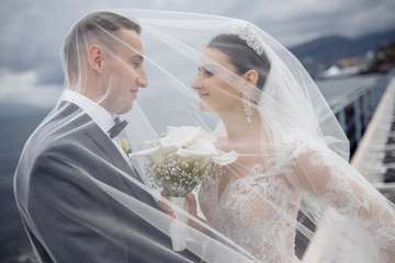 Beautiful groom and bride with long veil near the blue lake 