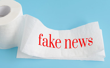 text fake news on white toilet paper on blue background, concept of lie in social media during coronavirus pandemic in the world