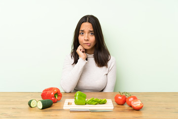 Young brunette woman with vegetables having doubts and with confuse face expression