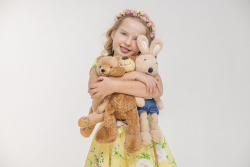 Girl with her toys bunny and teddy bear clutches toys and smiles at camera on isolated white