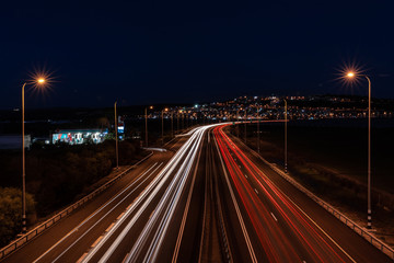 Long exposure image of cars rushing over a highway, with two lanterns on the sides, against the backdrop of the light from the Arab village.